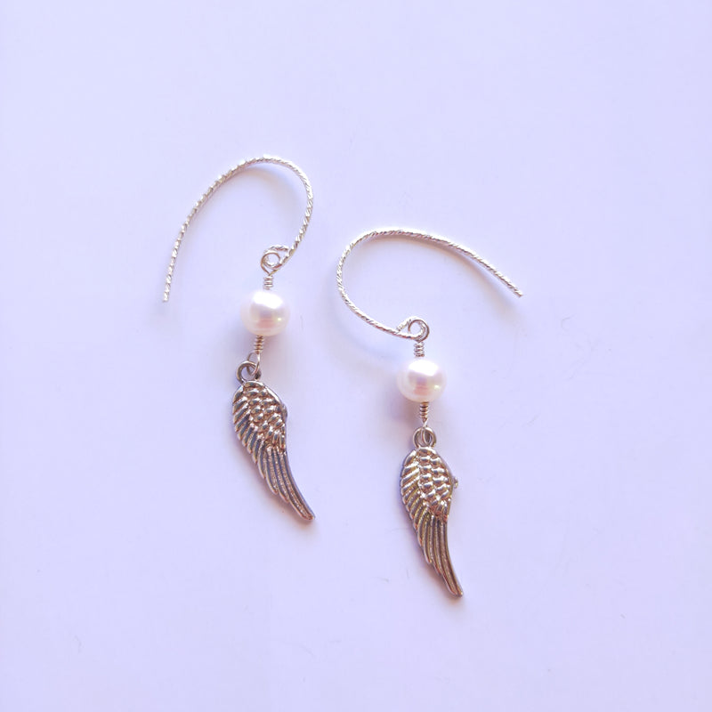 Silver angel wing earrings with pearl beads on a light purple background